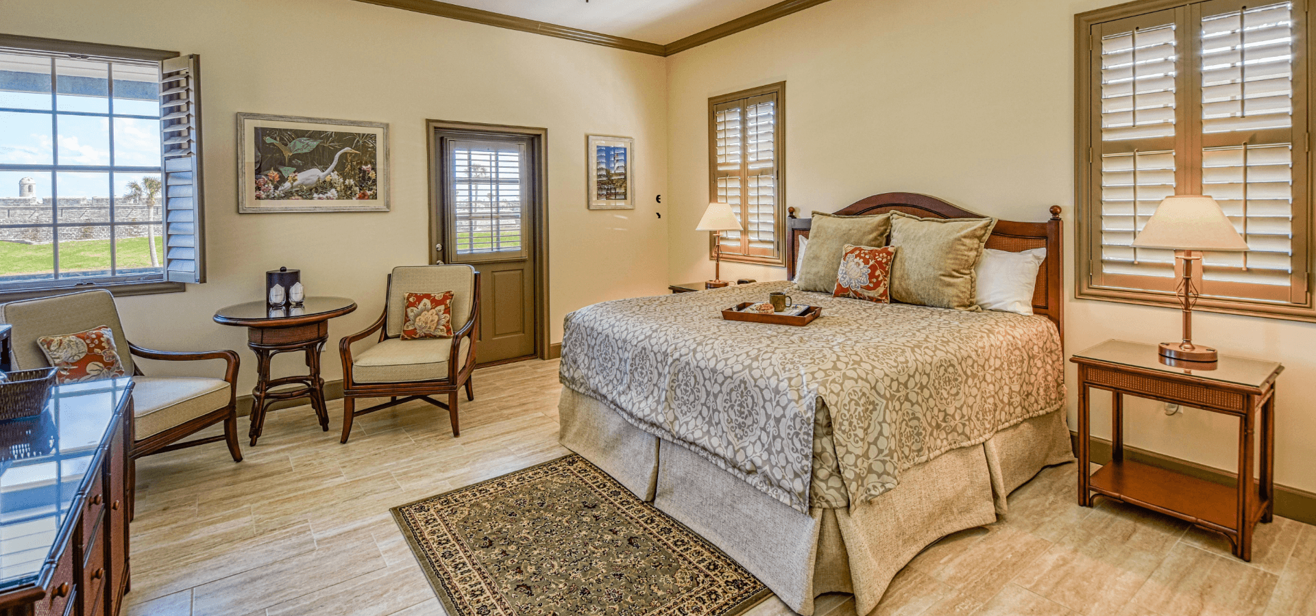 A cozy bedroom with a large bed, reading chairs, and natural light streaming through the window.
