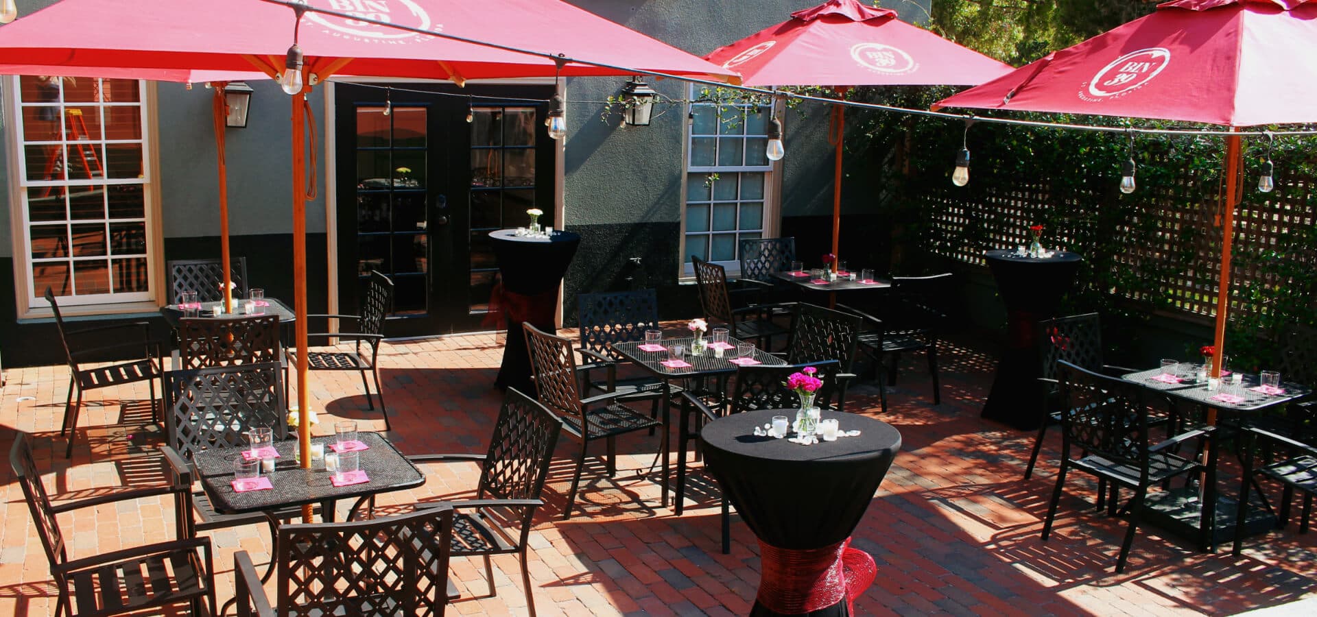 Outdoor dining area with black tables, red umbrellas, and planters.
