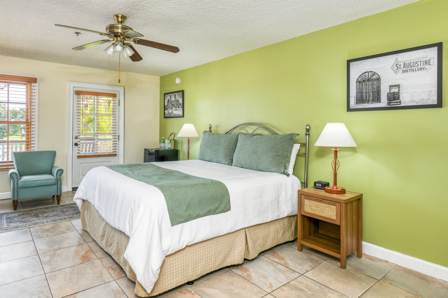 A cozy hotel room featuring a king-size bed, green walls, and a small seating area with a chair.