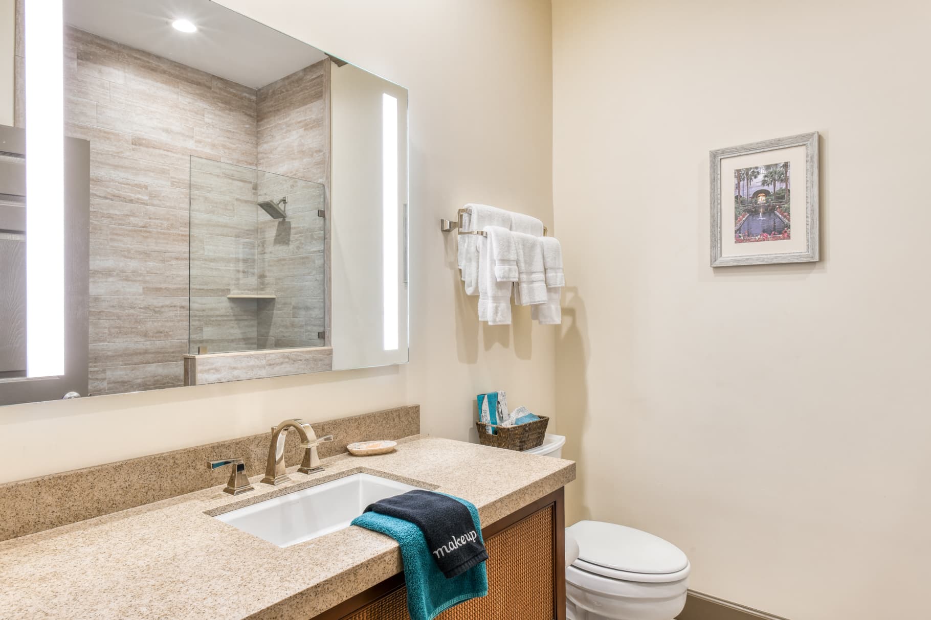 A modern bathroom featuring a sink with a granite countertop, a glass shower, and neatly arranged towels.