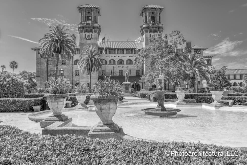 A black and white image of a historic building surrounded by palm trees and landscaped gardens.