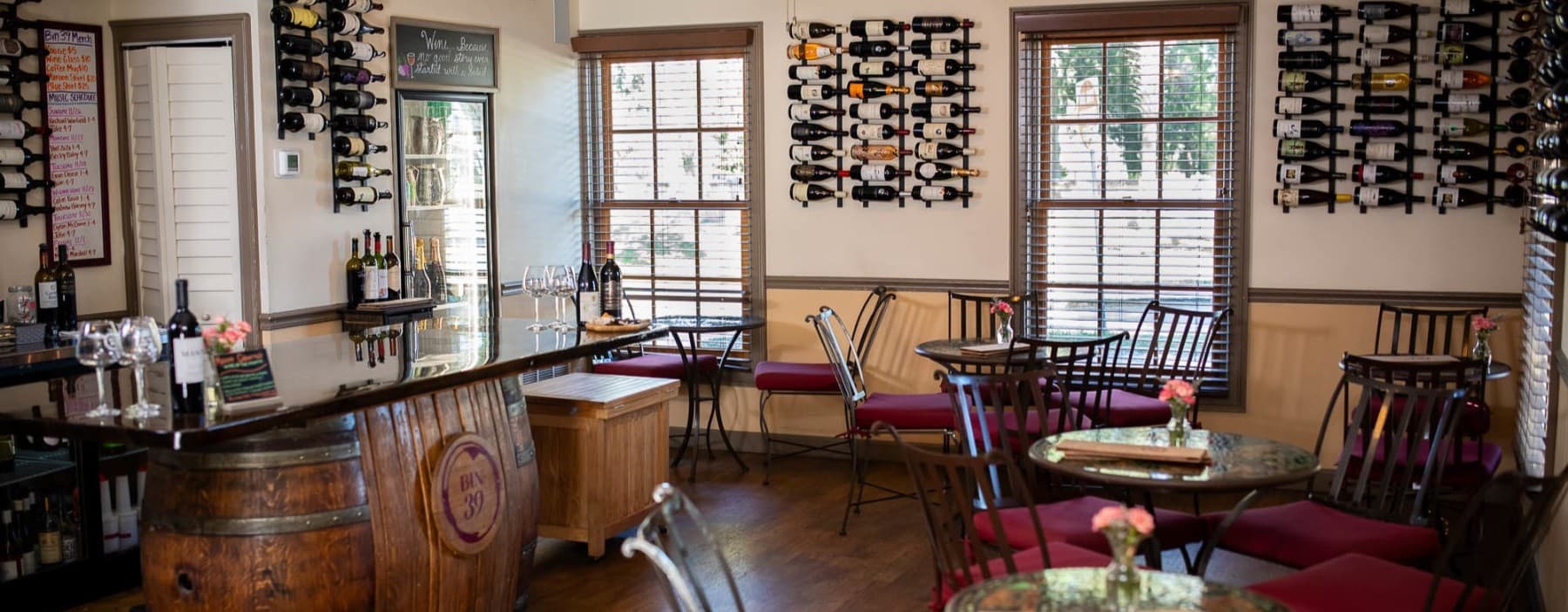 A cozy wine bar featuring a wooden counter, scattered tables, and walls adorned with wine bottles.