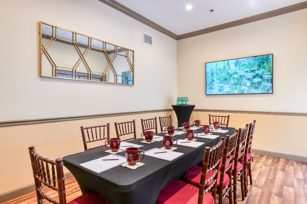 A conference room set for a meeting, featuring a long table, chairs, coffee mugs, and a large decorative mirror and screen.