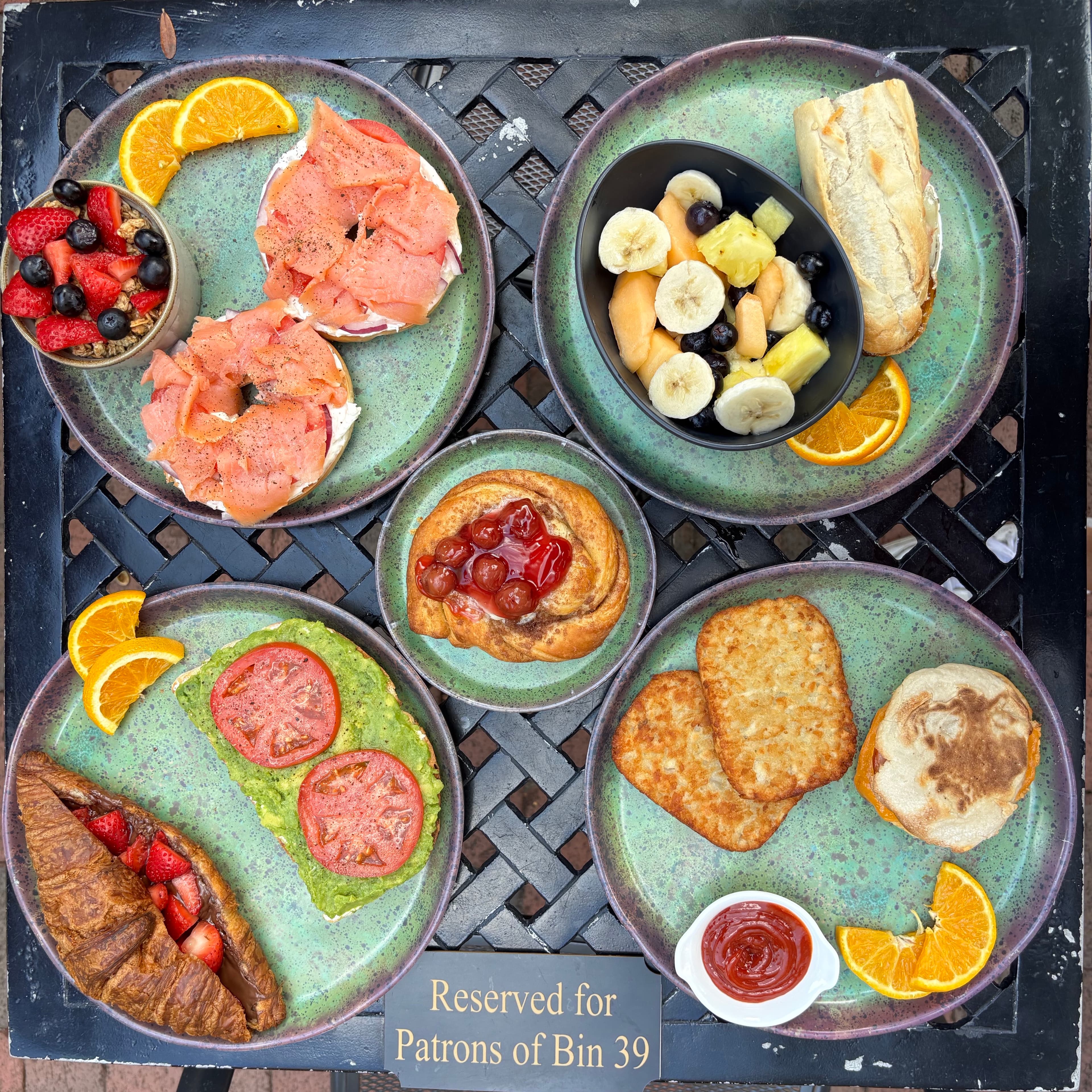 A variety of breakfast dishes, including smoked salmon, fruit, croissants, and pastries, arranged on green plates.