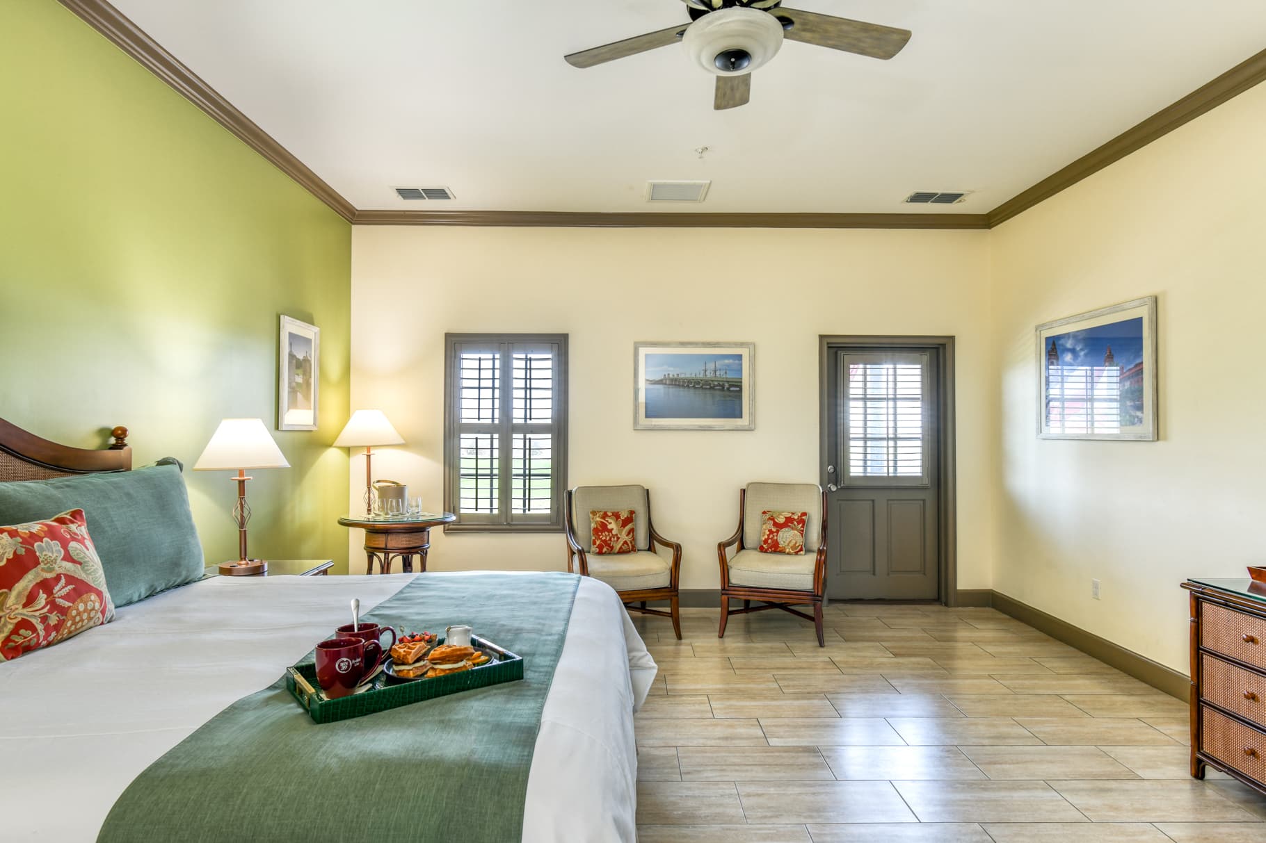 A bright, spacious hotel room featuring a king-sized bed, seating area, and decorative accents in green and beige.