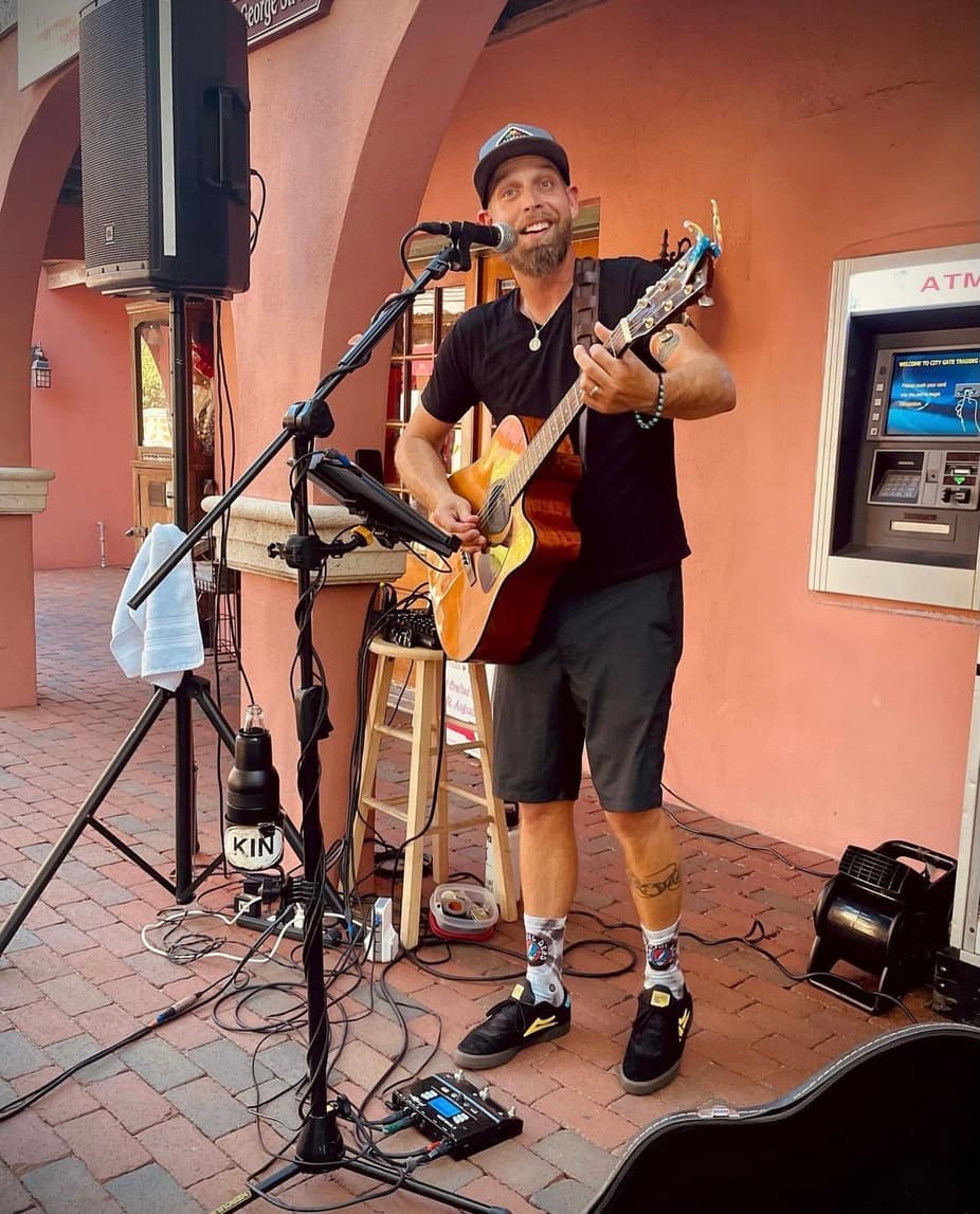 A musician with an acoustic guitar performs lively on a small outdoor stage.