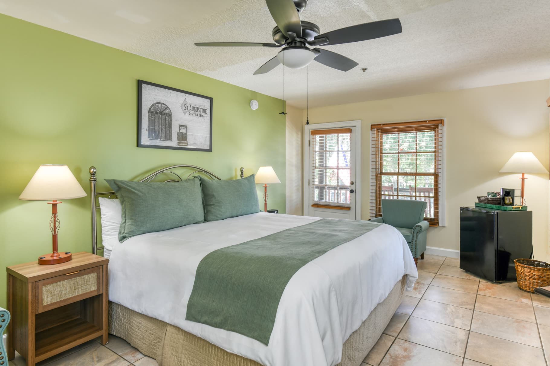 A cozy hotel room featuring a king-sized bed, green accent wall, and bright natural light from windows.