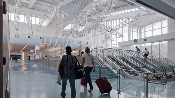 A modern airport interior featuring escalators and colorful hanging art.