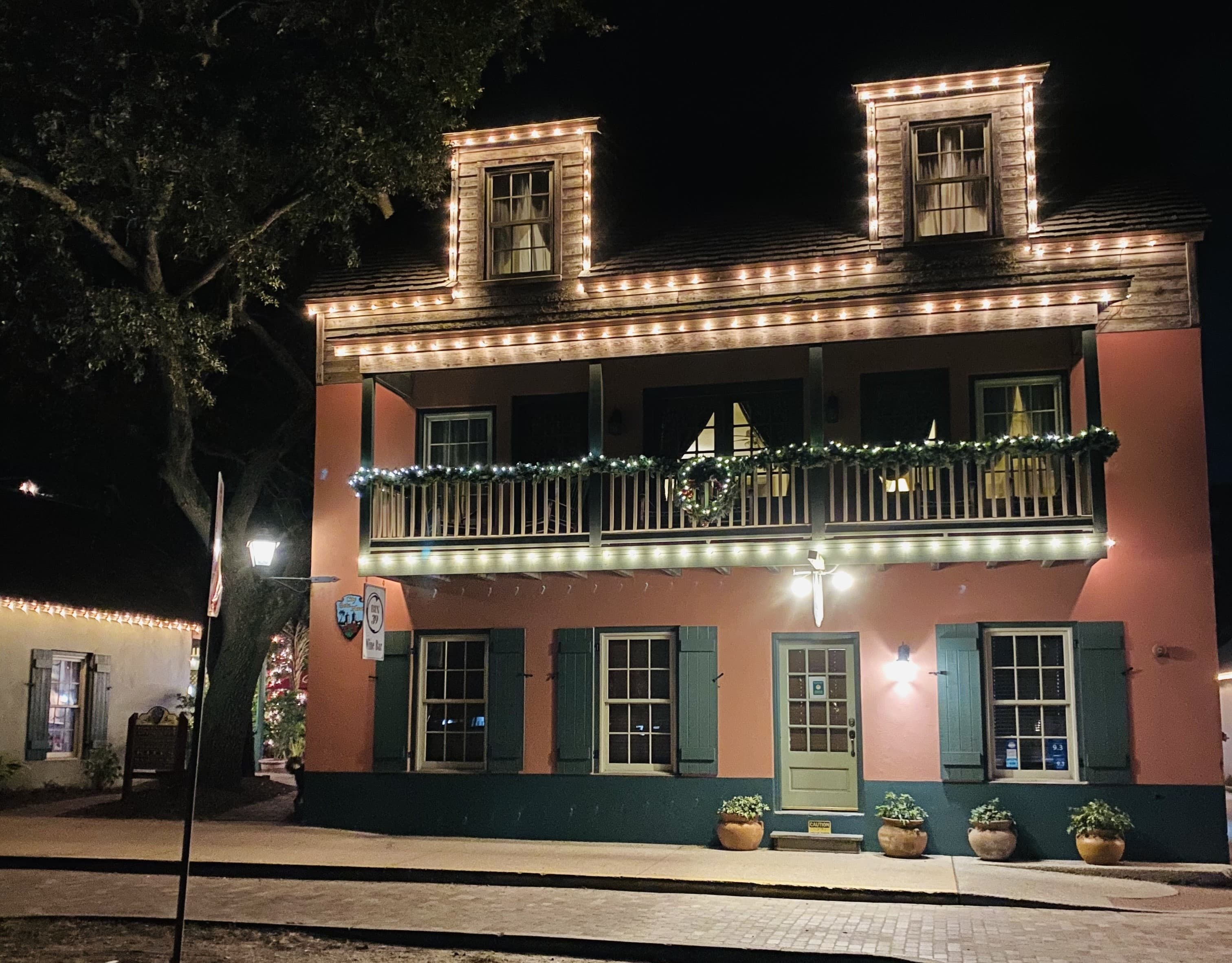 A pink building adorned with festive lights and greenery at night.
