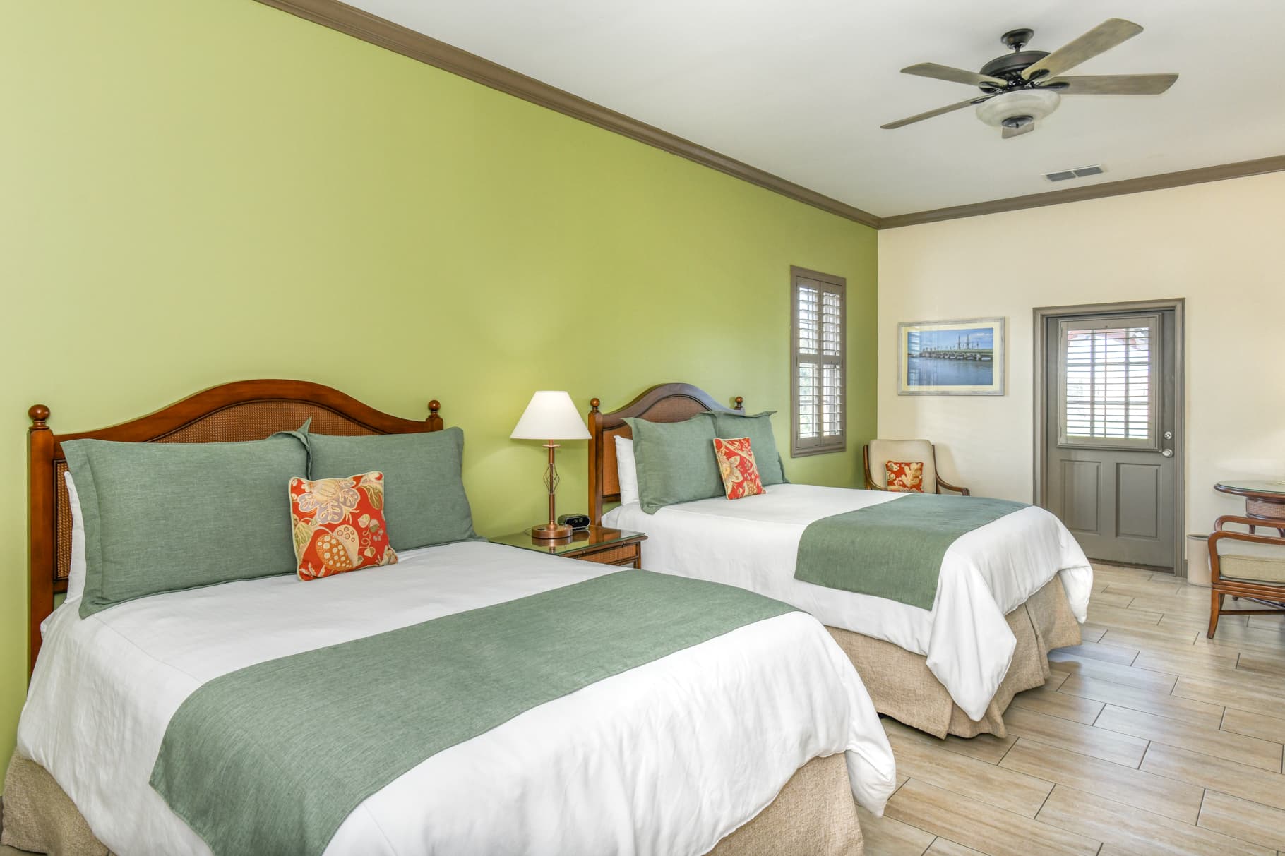 A cozy guest room featuring two double beds with green accents and a light green wall.