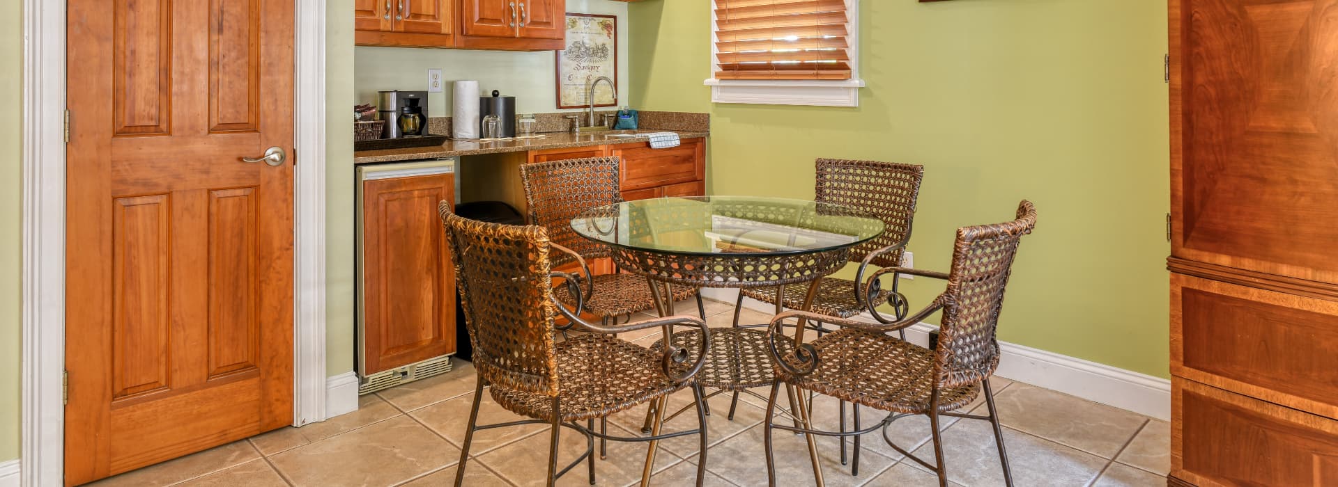A small kitchen area featuring a glass-topped table surrounded by woven chairs and wooden cabinets.