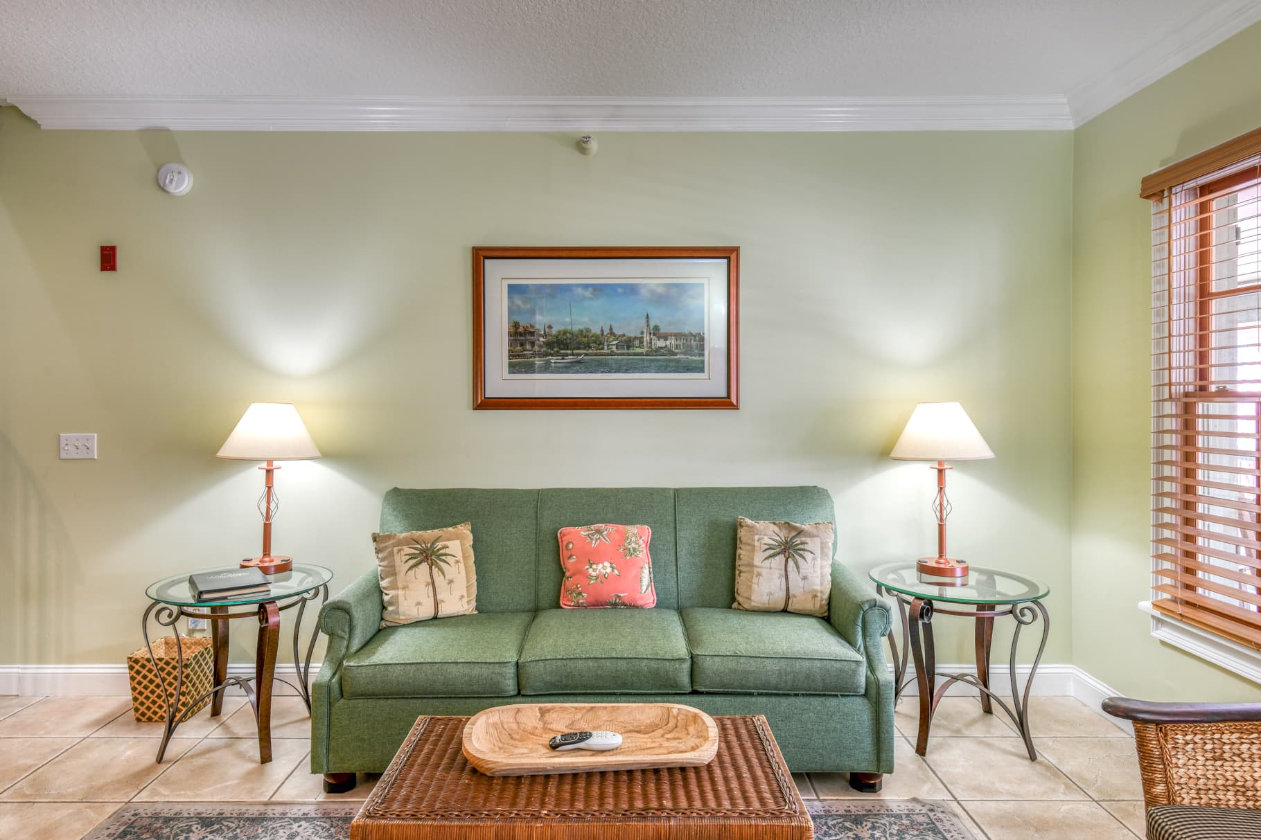 Cozy living room featuring a green sofa, decorative pillows, and side tables with lamps against a light green wall.