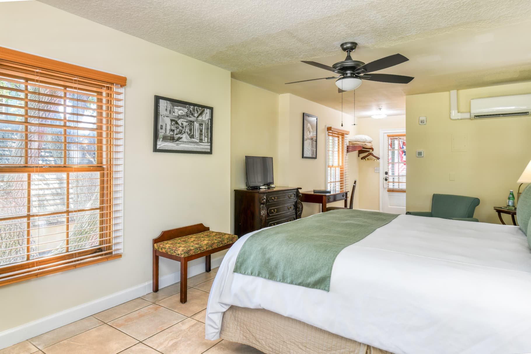 A cozy bedroom featuring a king-sized bed, a television, and large windows with wooden blinds.