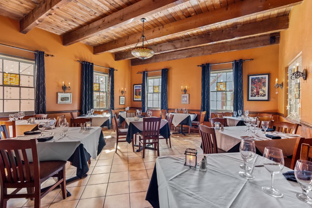 A cozy restaurant interior featuring wooden beams, orange walls, and neatly set tables.