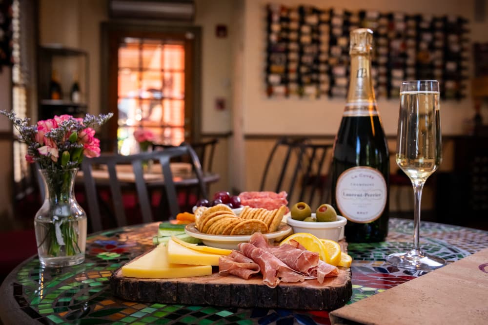 A table set with charcuterie, cheese, crackers, olives, and sparkling wine, complemented by a small vase of flowers.