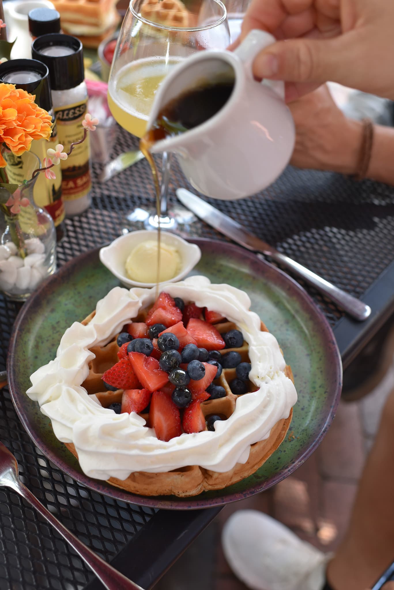 A waffle topped with whipped cream and mixed berries, with syrup being poured over it.