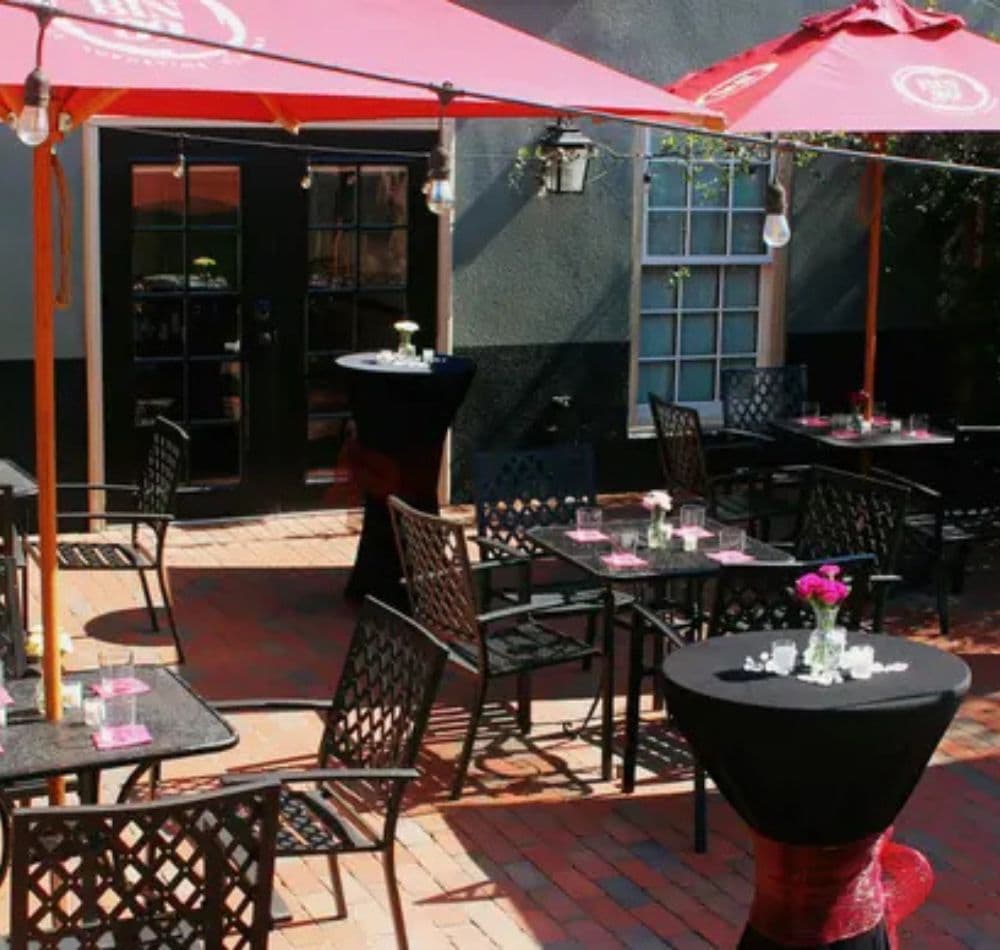 Outdoor dining area with tables under red umbrellas and potted flowers.