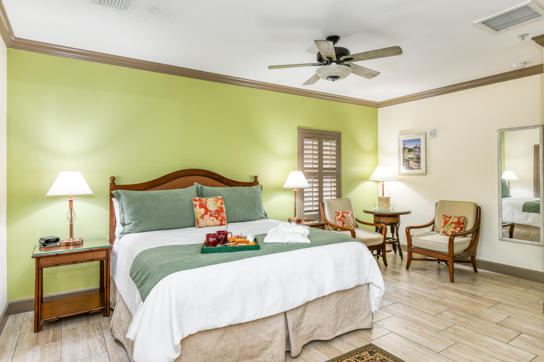 Cozy bedroom with green walls featuring a king-sized bed, two chairs, and warm lighting.