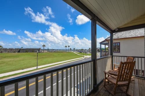 View from a balcony overlooking a grassy area and road, with palm trees and a bright blue sky.