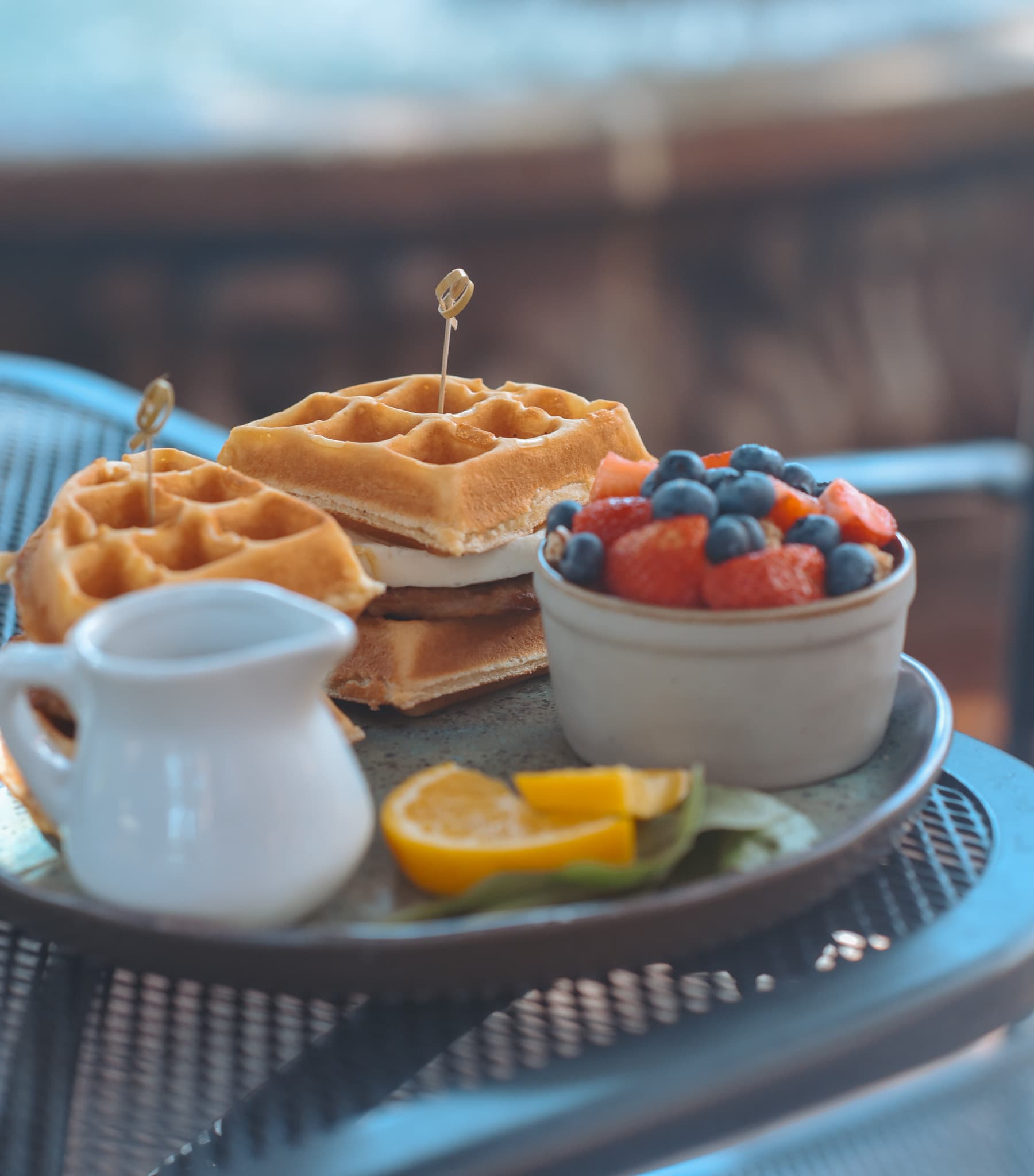 A plate featuring stacked waffles with a drizzle of syrup, accompanied by a bowl of mixed berries and citrus slices.