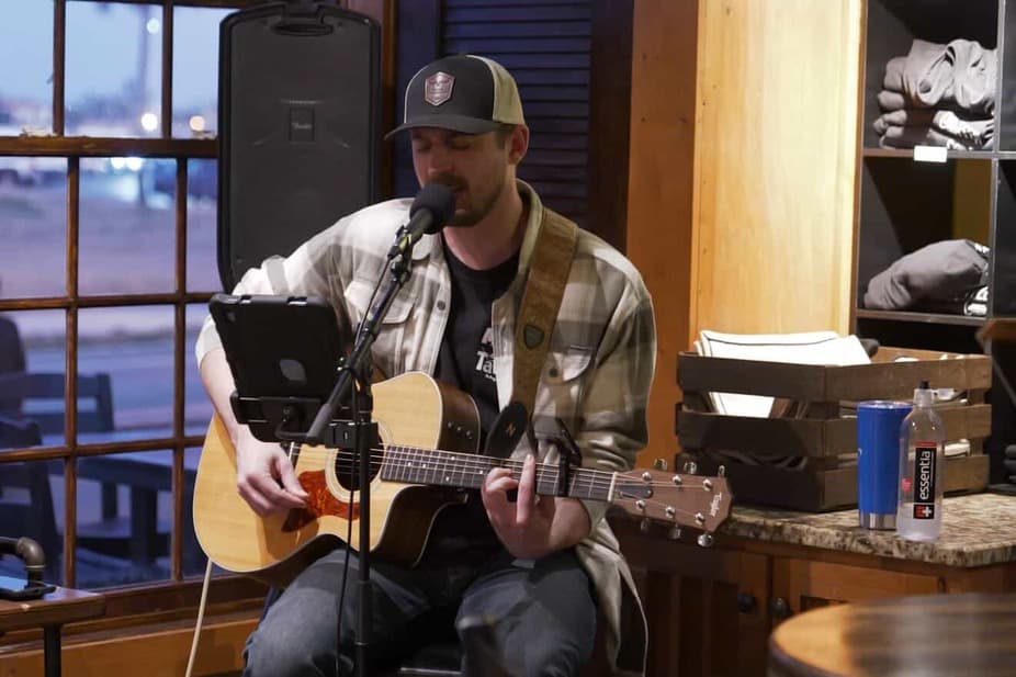 A musician plays guitar and sings into a microphone at a cozy venue.
