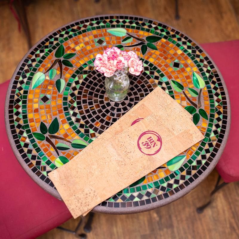 A vibrant mosaic table with a small vase of pink flowers and a folded menu.