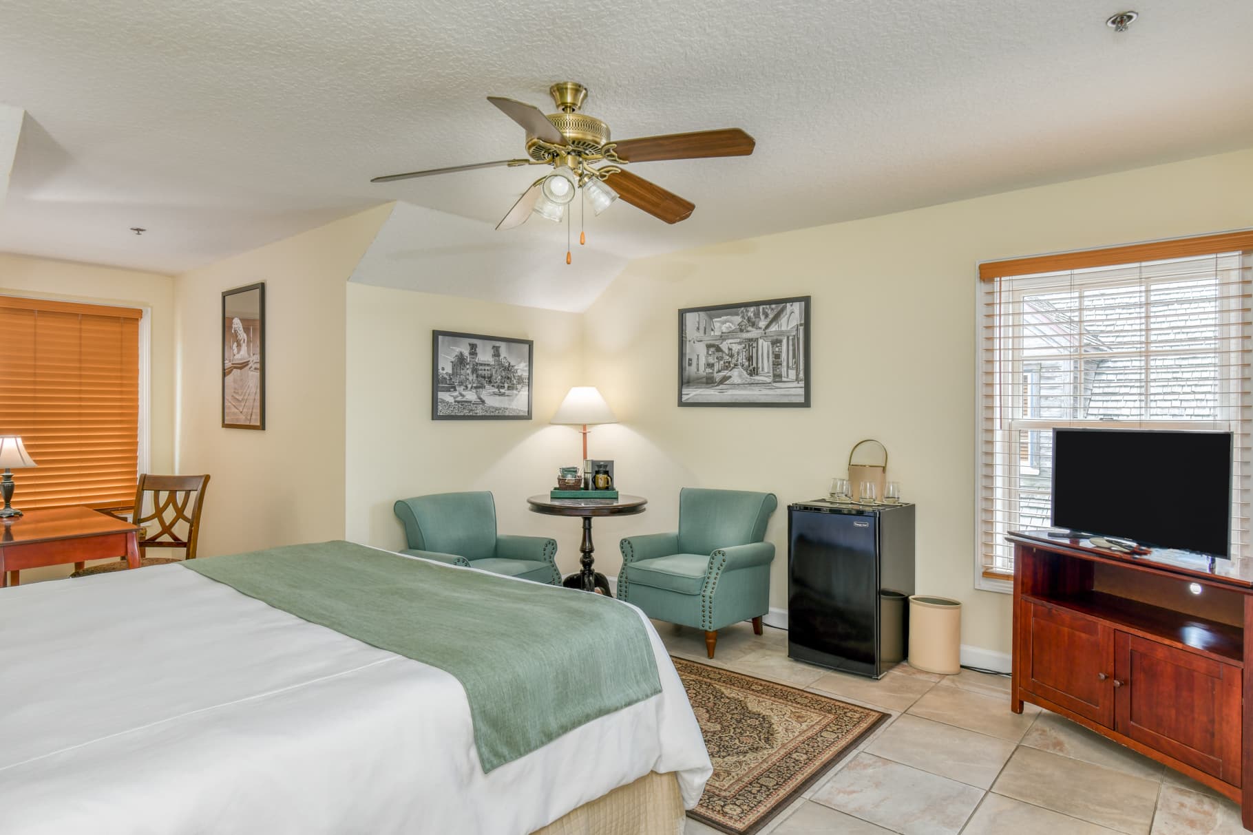 A cozy hotel room featuring a queen bed, two armchairs, a small dining area, and a television.