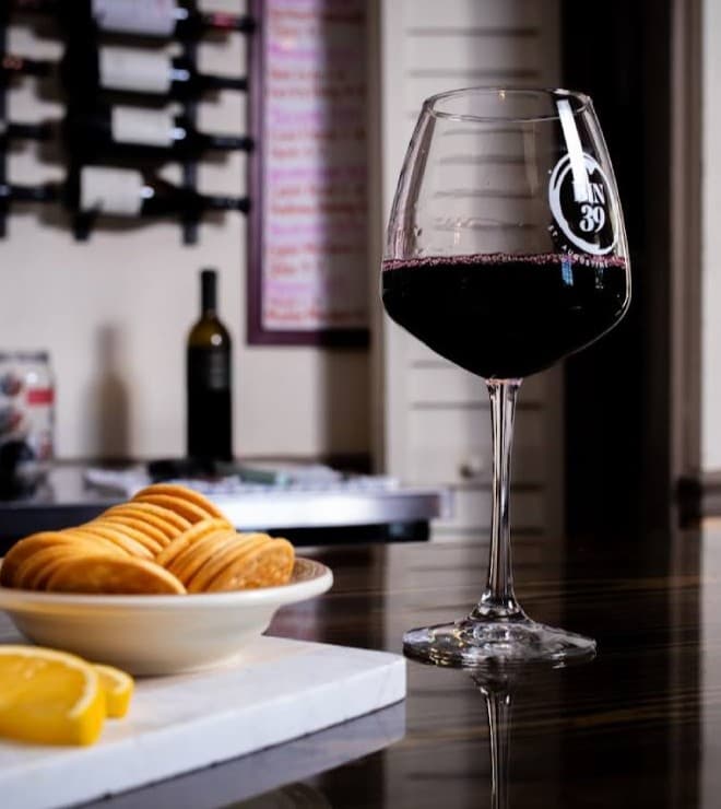 A glass of red wine beside a plate of cookies and a lemon wedge on a table.