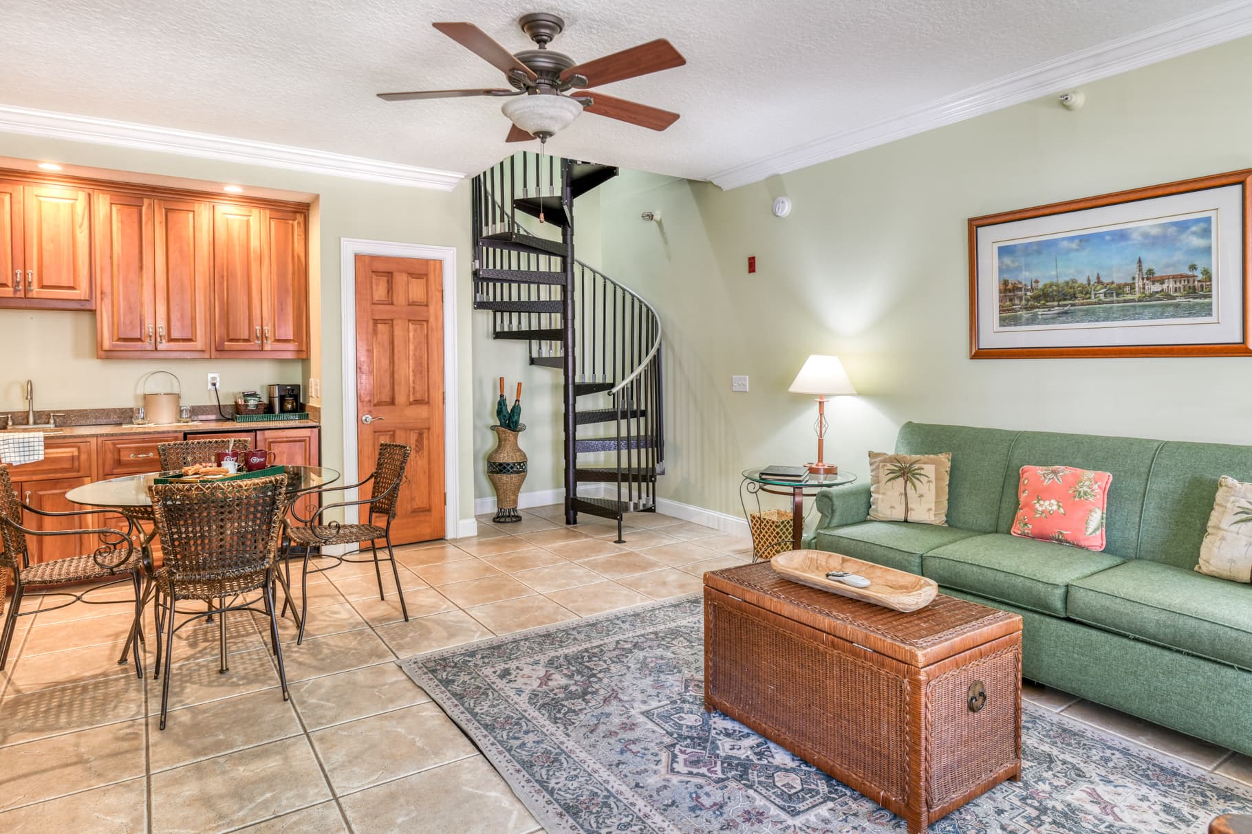 A cozy living area featuring a green sofa, a wooden coffee table, dining set, and a spiral staircase.