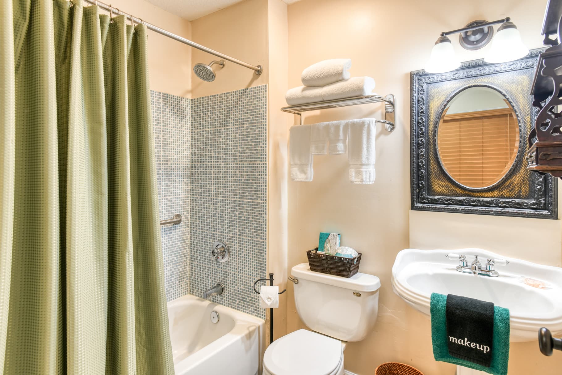 A compact bathroom featuring a shower curtain, bathtub, sink, and decorative mirror.