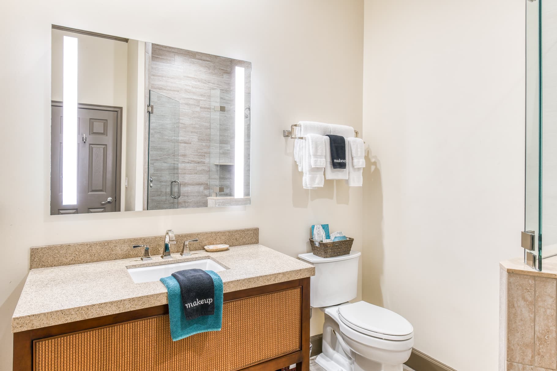 A modern bathroom featuring a sink with a wooden vanity, large mirror, glass shower, and neatly arranged towels.