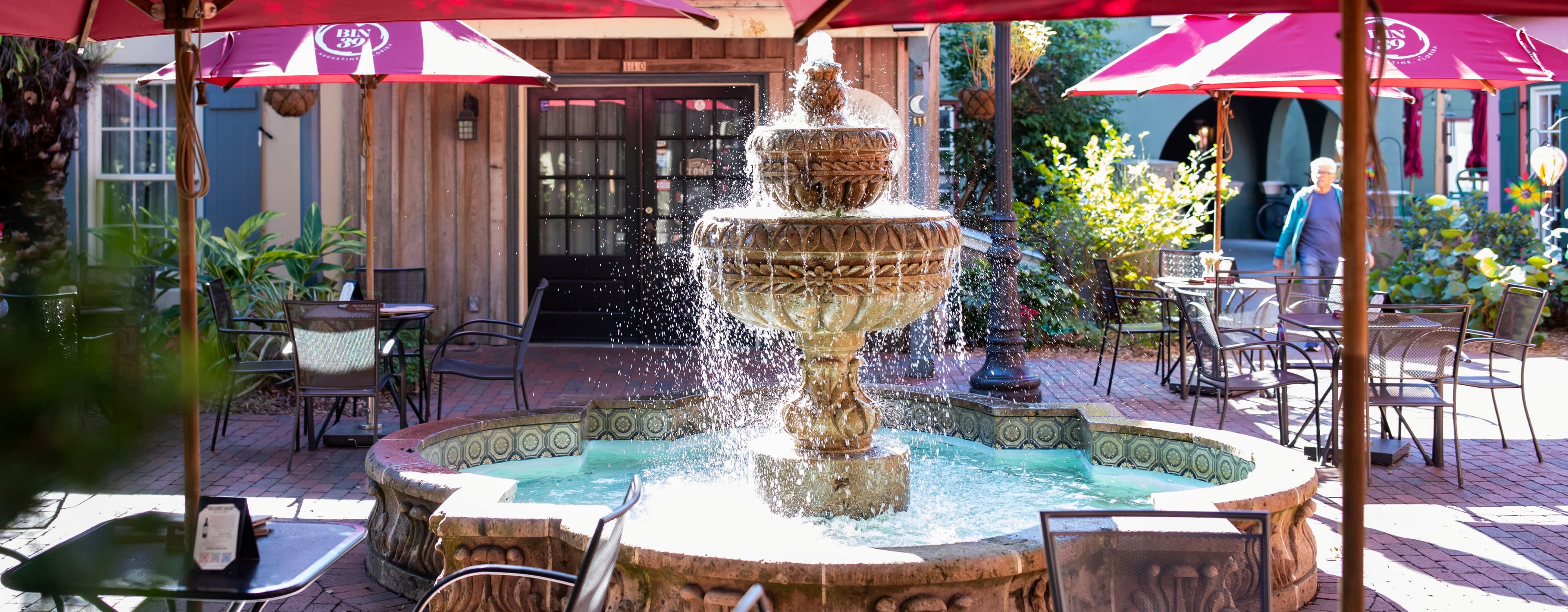 A decorative fountain surrounded by outdoor seating and umbrellas in a charming courtyard.