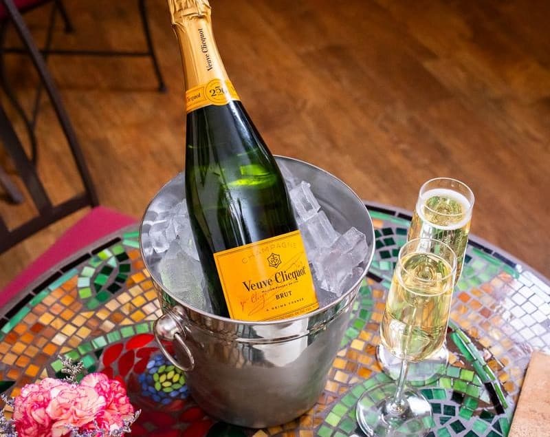 A bottle of Veuve Clicquot champagne in an ice bucket with two filled flutes on a colorful table.
