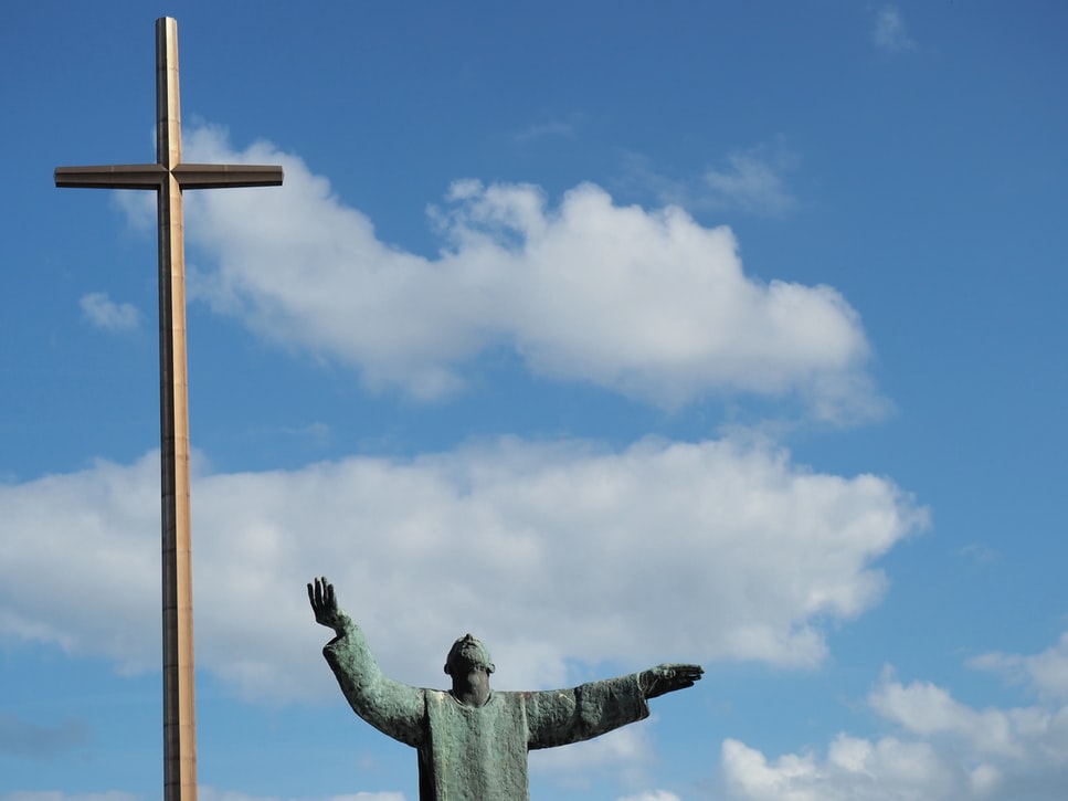 Large metal cross and green rusted statue at Cathedral Basilica of St. Augustine against a partly cloudy sky